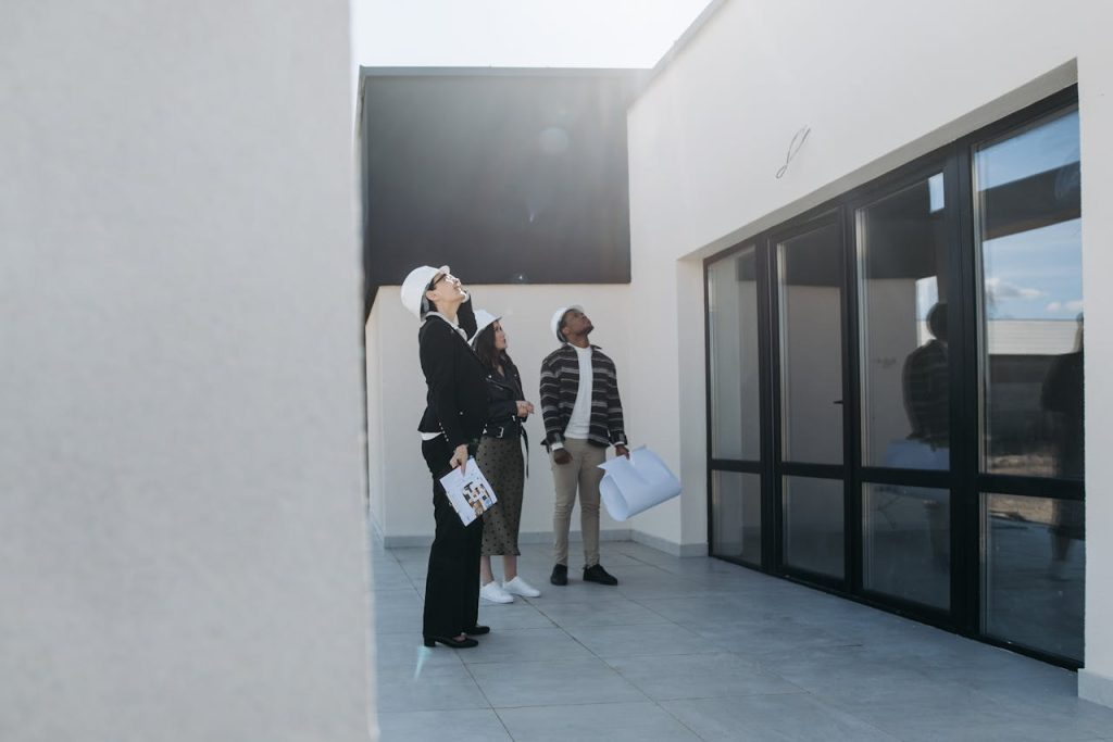 clients-and-real-estate-agent-looking-at-roof-of-house-for-sale-7937732 Group of real estate agents assessing a modern building during the day.