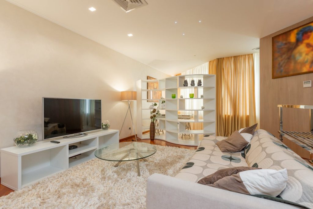 interior-of-modern-living-room-with-tv-on-cabinet-on-cozy-couch-7147284 Glass round coffee table placed on soft fur rug between comfortable sofa and modern TV set in spacious living room