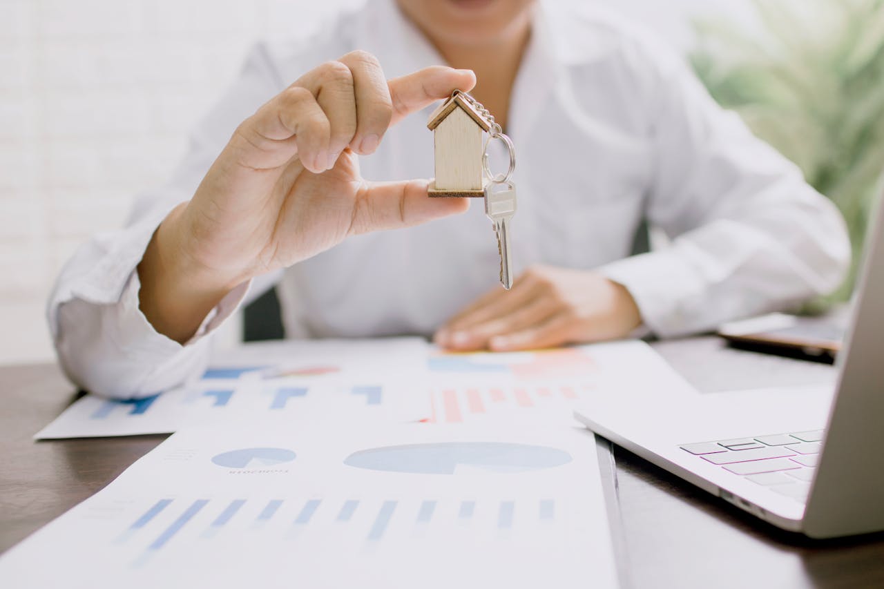 woman-in-white-long-sleeve-shirt-holding-silver-and-gold-framed-eyeglasses-4161619 Real estate professional presenting a house model with keys, symbolizing property investment and ownership.