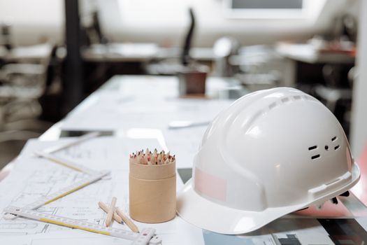 pexels-photo-5583255-5583255 Close-up von an office desk with a white helmet, colored pencils, and architectural plans.